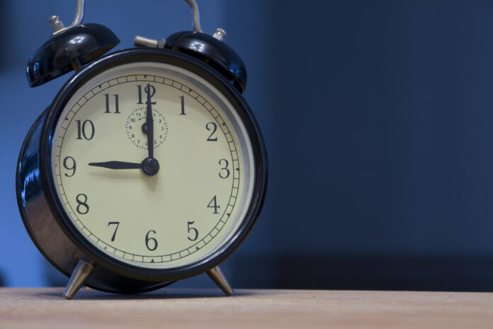 Vintage and retro analogue alarm clock indicating that it's nine o' clock, 9pm or 9am, on a dark blue background