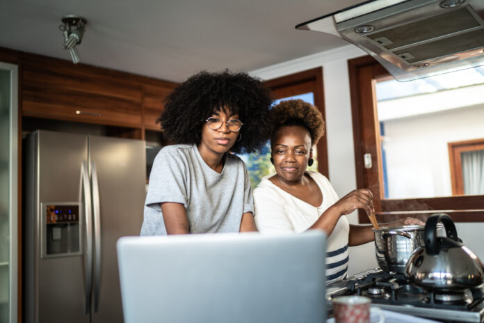 Mother and daughter cooking together and looking to laptop in the kitchen