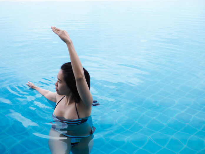 beautiful professional asian woman practice aqua yoga water therapy side bend twist pose balance in swimming pool body mind spirit spiritual healing