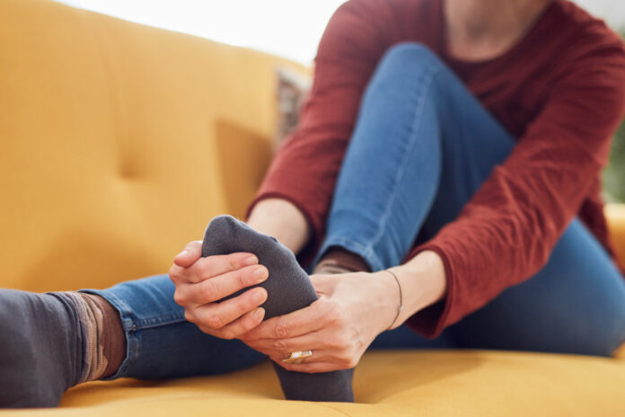 Woman with feet intense pain sitting on a couch at home.