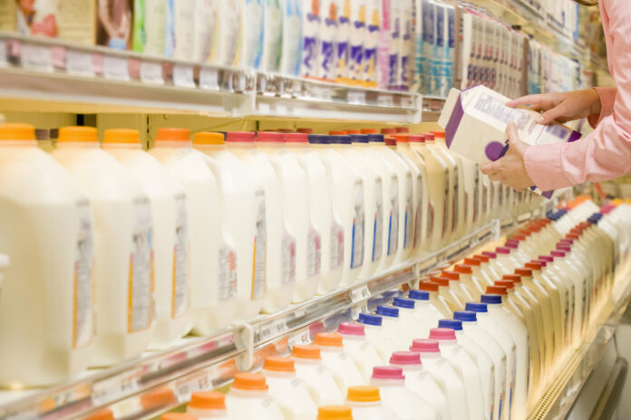 Woman checking ingredients on back of milk carton in supermarket A2 milk