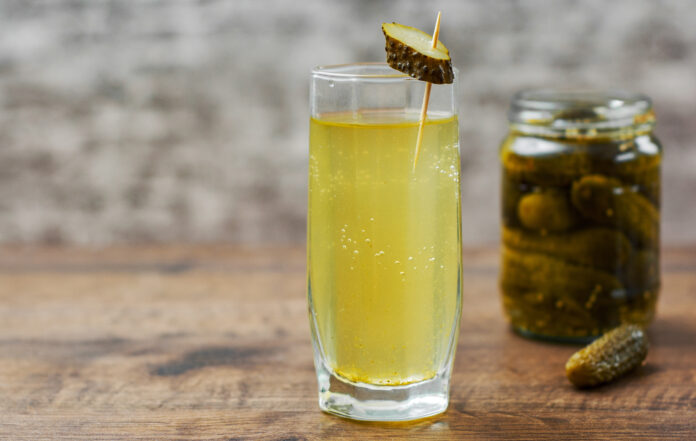 Pickle juice in glass and a can of pickled cucumbers on wooden table background Pickle juice for cramps