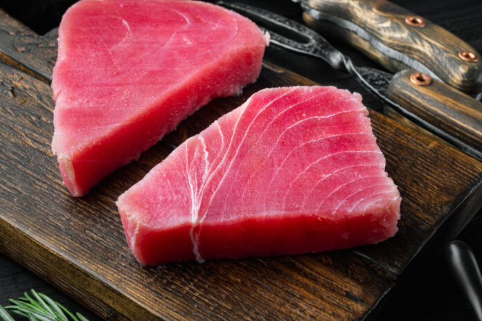 Raw tuna fillet. Seafood with sugar green pea, sesame and ingredients, on wooden cutting board, on black wooden background